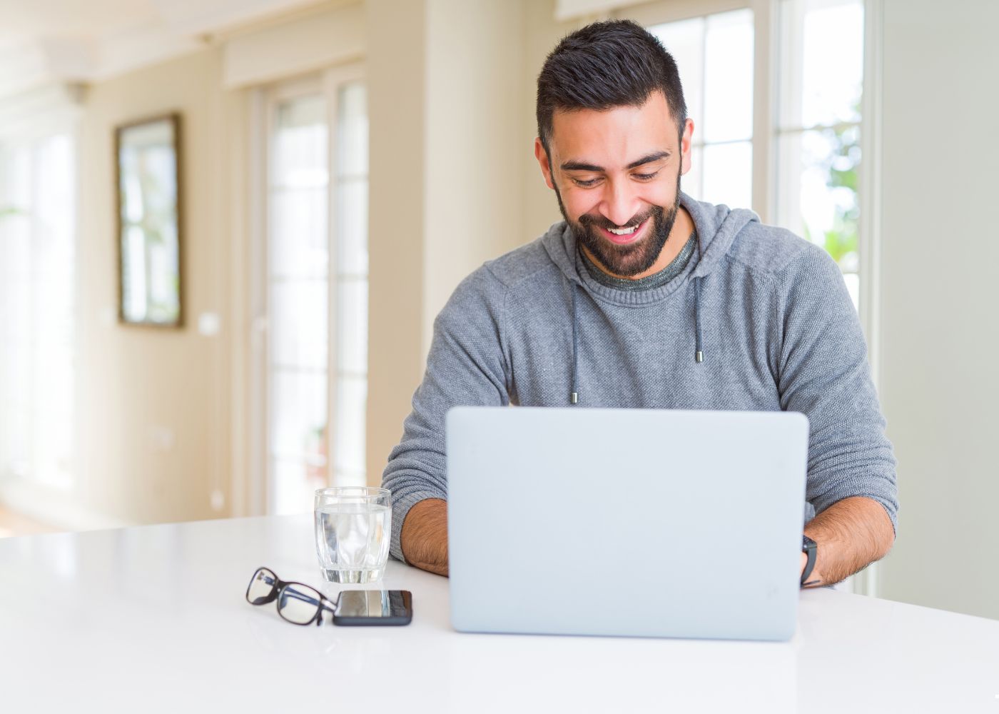 Smiling man wearing a grey sweater working on a laptop