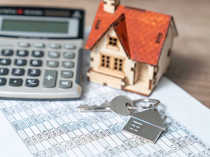 A small model house, a key and calculator on top of a paper with numbers. 