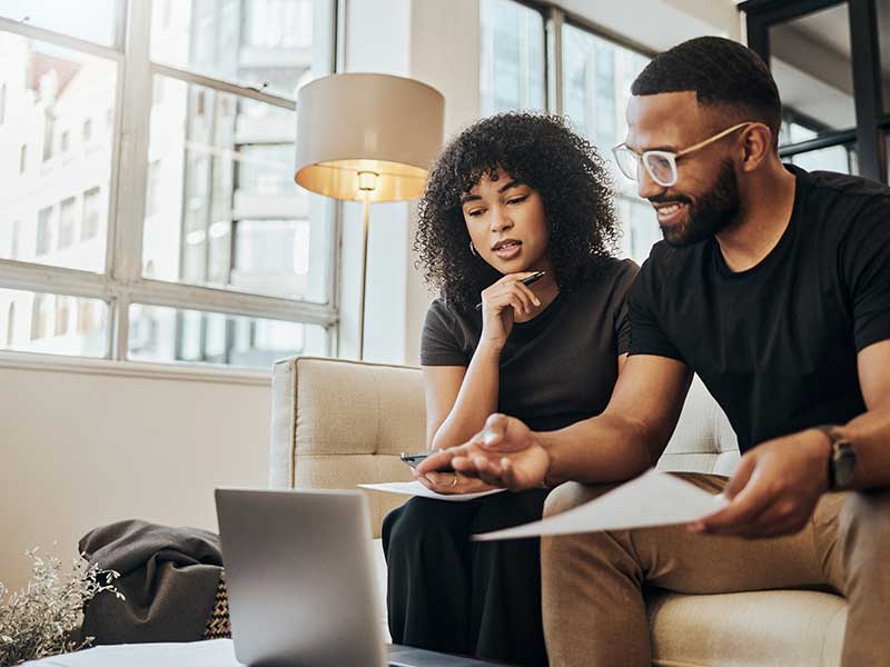 A couple at home sitting on the sofa looking at a laptop.