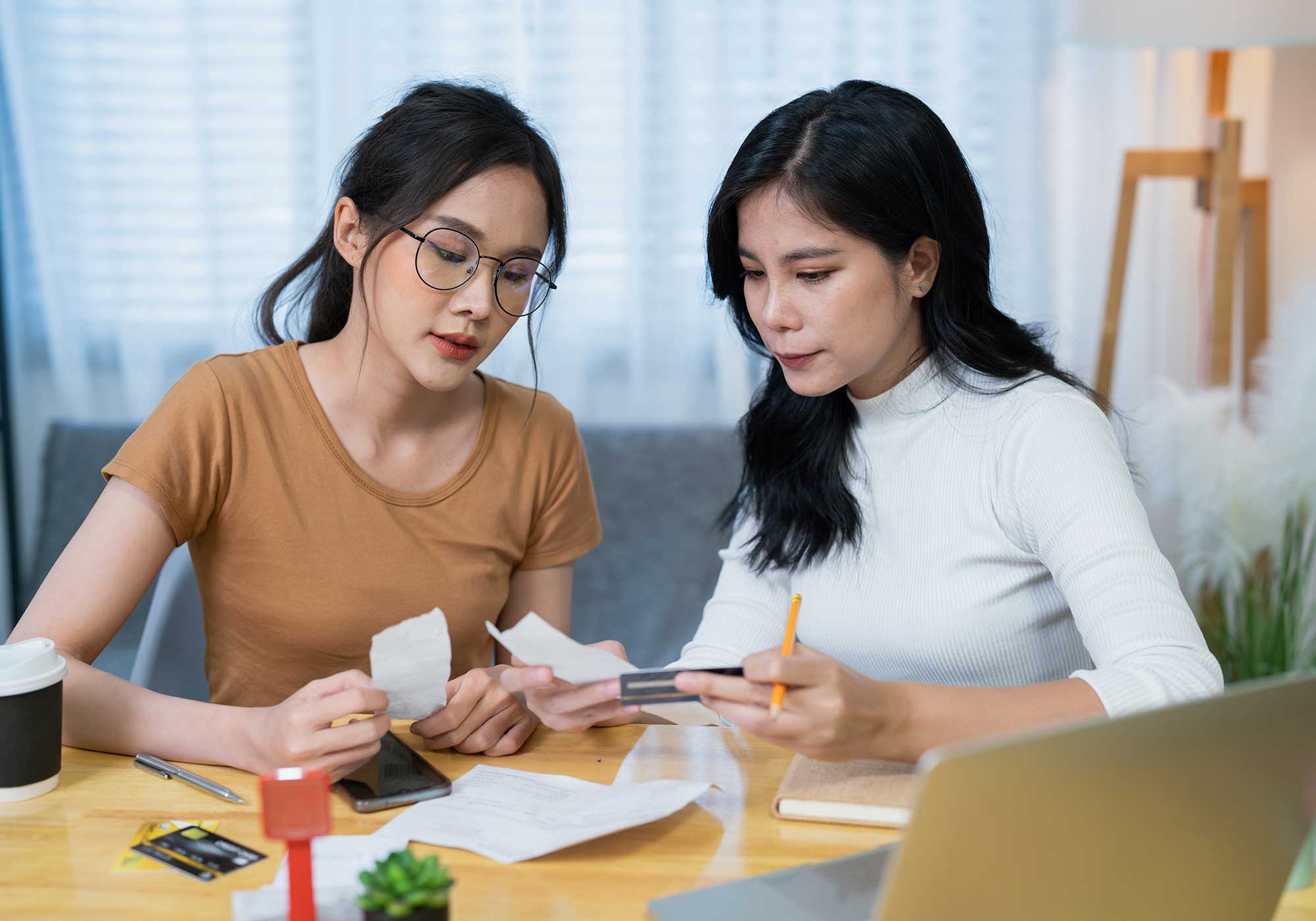 Two woman sitting at a table looking at receipts and holding a credit card. 