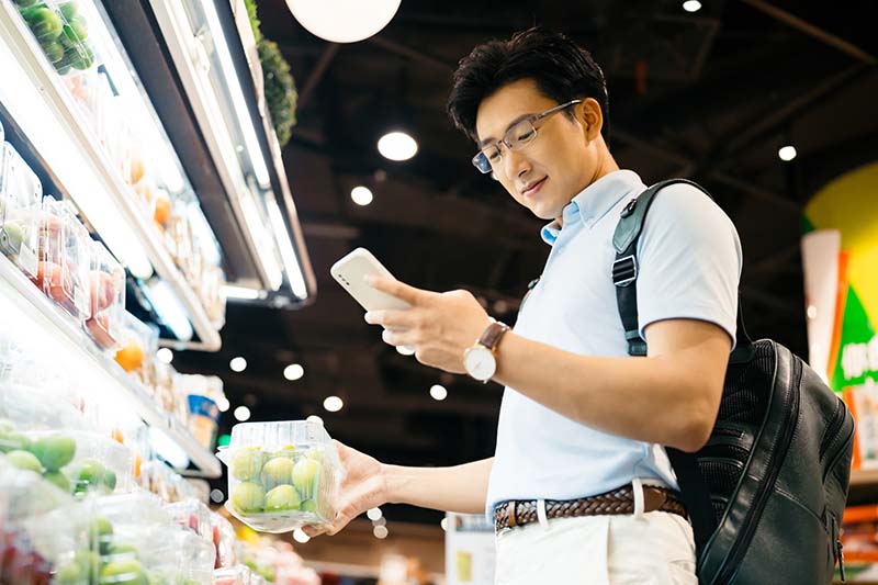 man shopping at grocery store while looking at phone