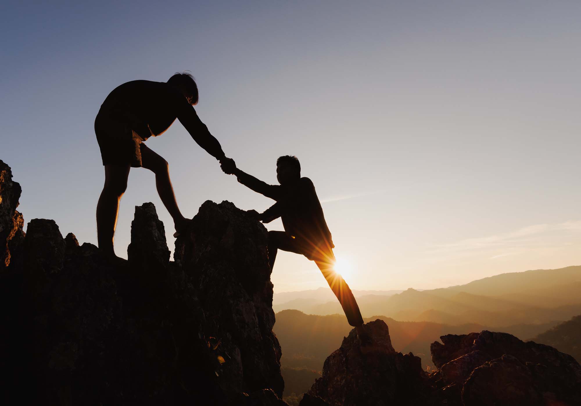 man standing on mountain helping another man climb up