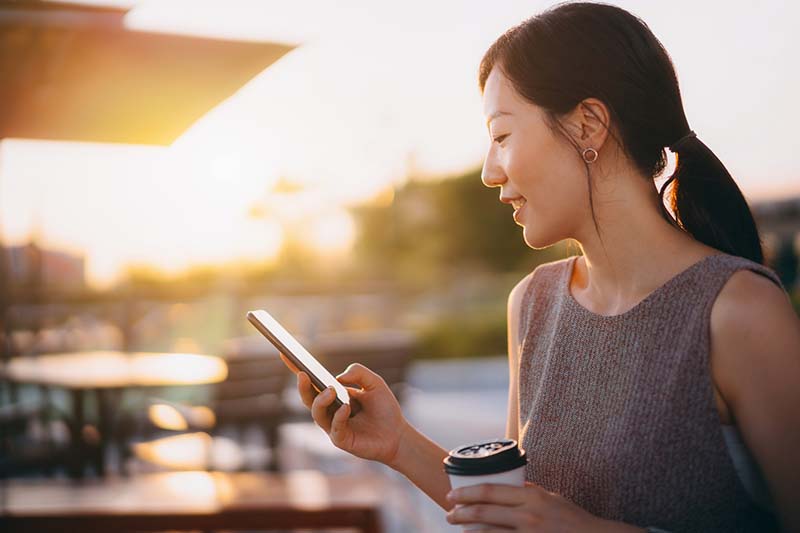 woman outside holding cup of coffee while looking at phone