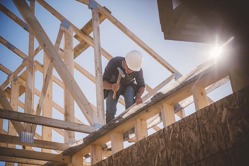 Construction worker hammering frame of house. 