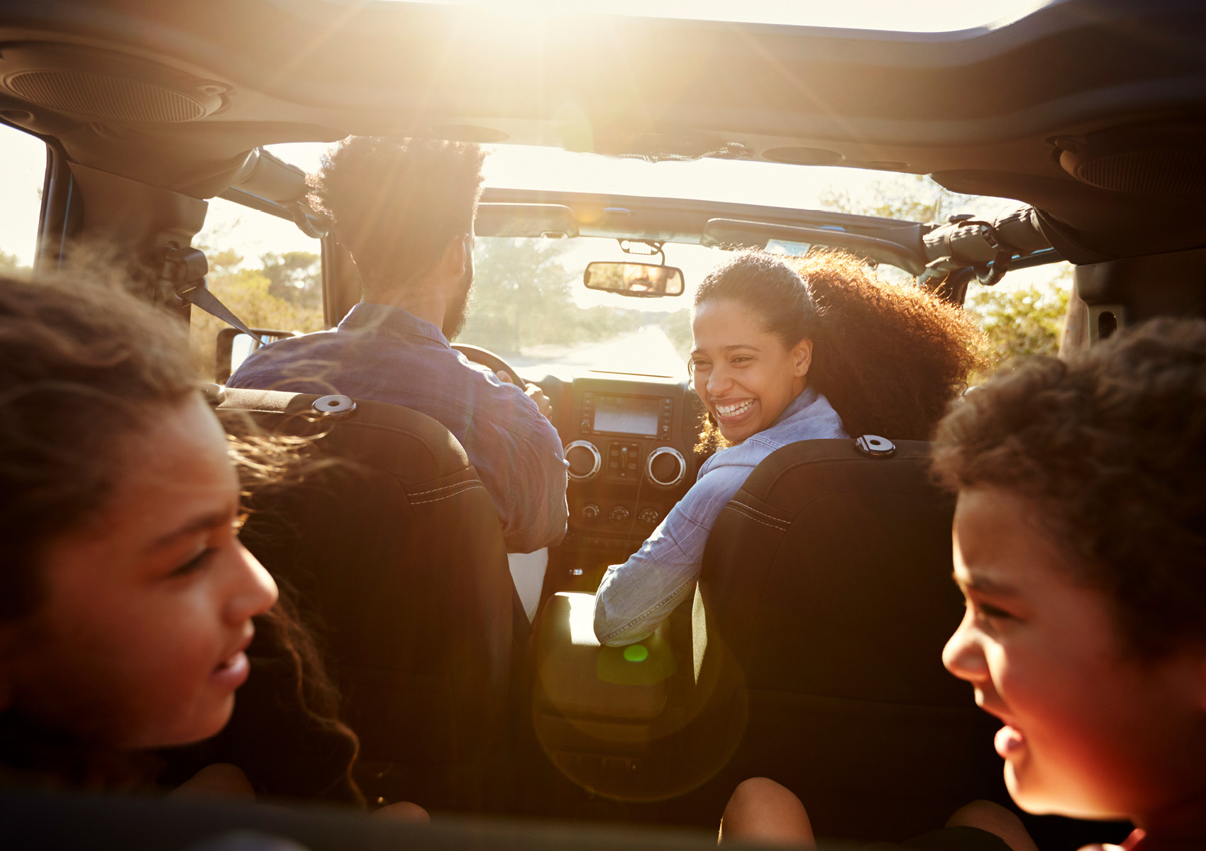 A happy family in the car driving and mother looking back at children.