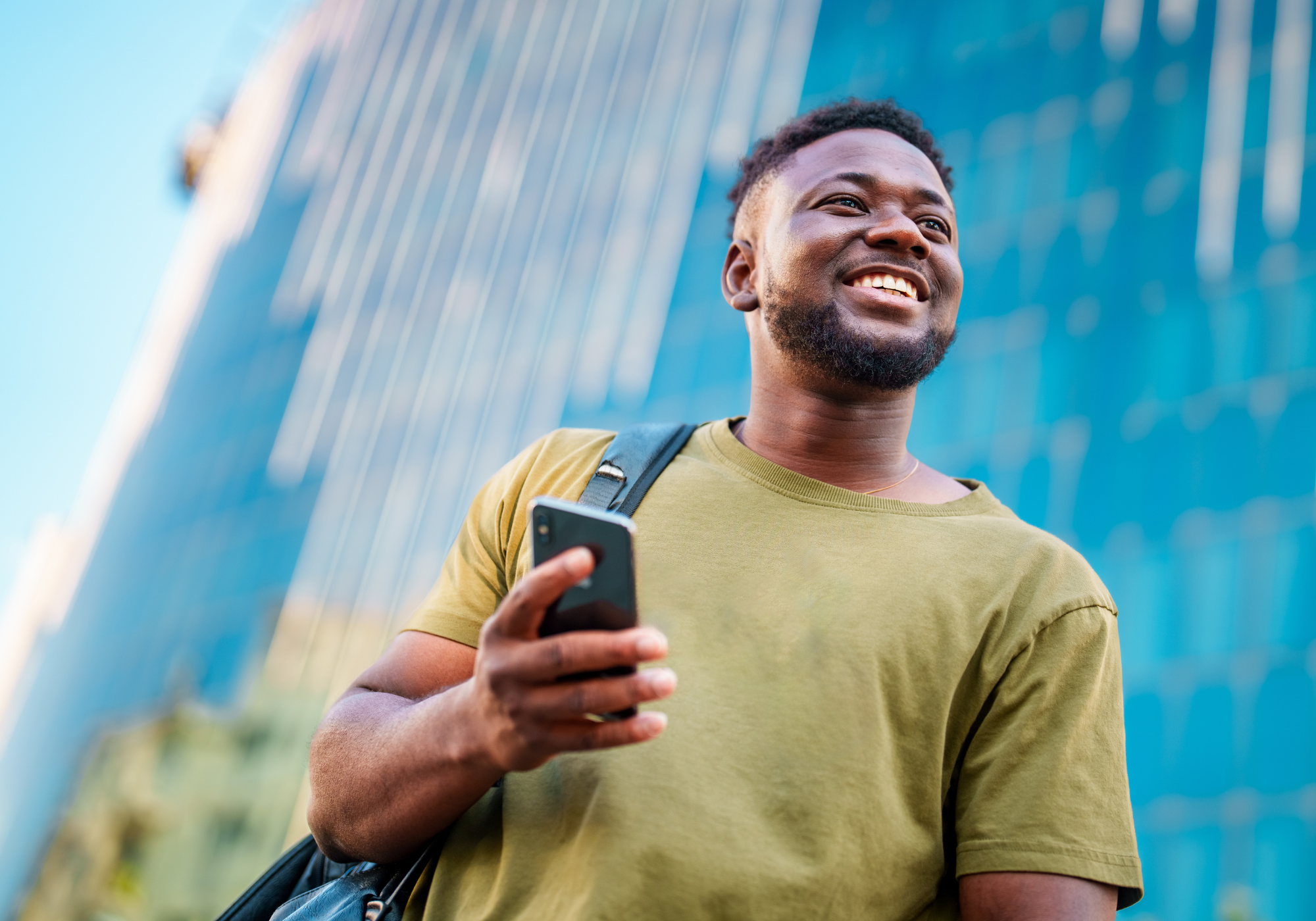 Confident young man in urban setting holding smartphone and looking hopeful