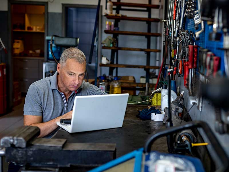 Man in autoshop looking at his laptop. 