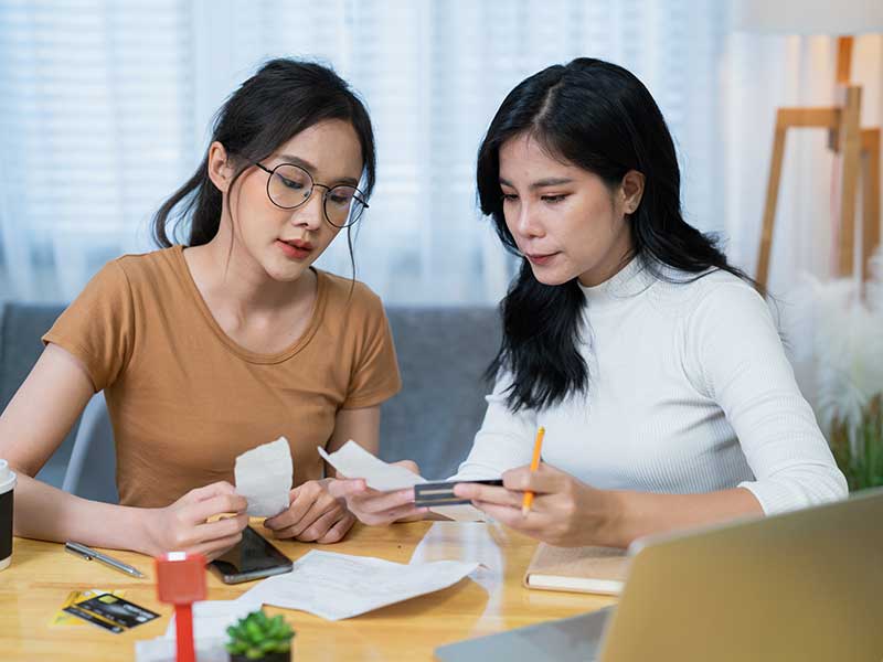 Two women sitting down looking at receipts, while one woman is holding her The Police Credit Union credit card.