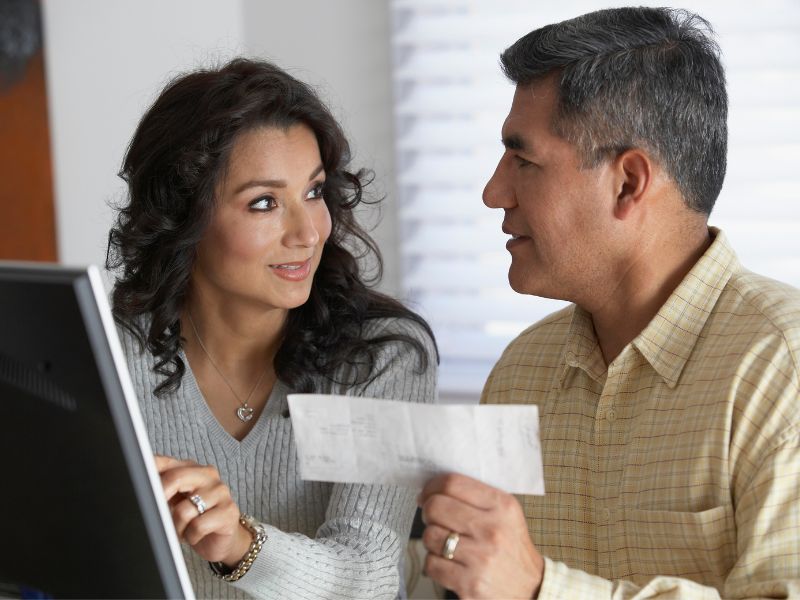 Woman pointing to computer screen looking at man holding a check. 