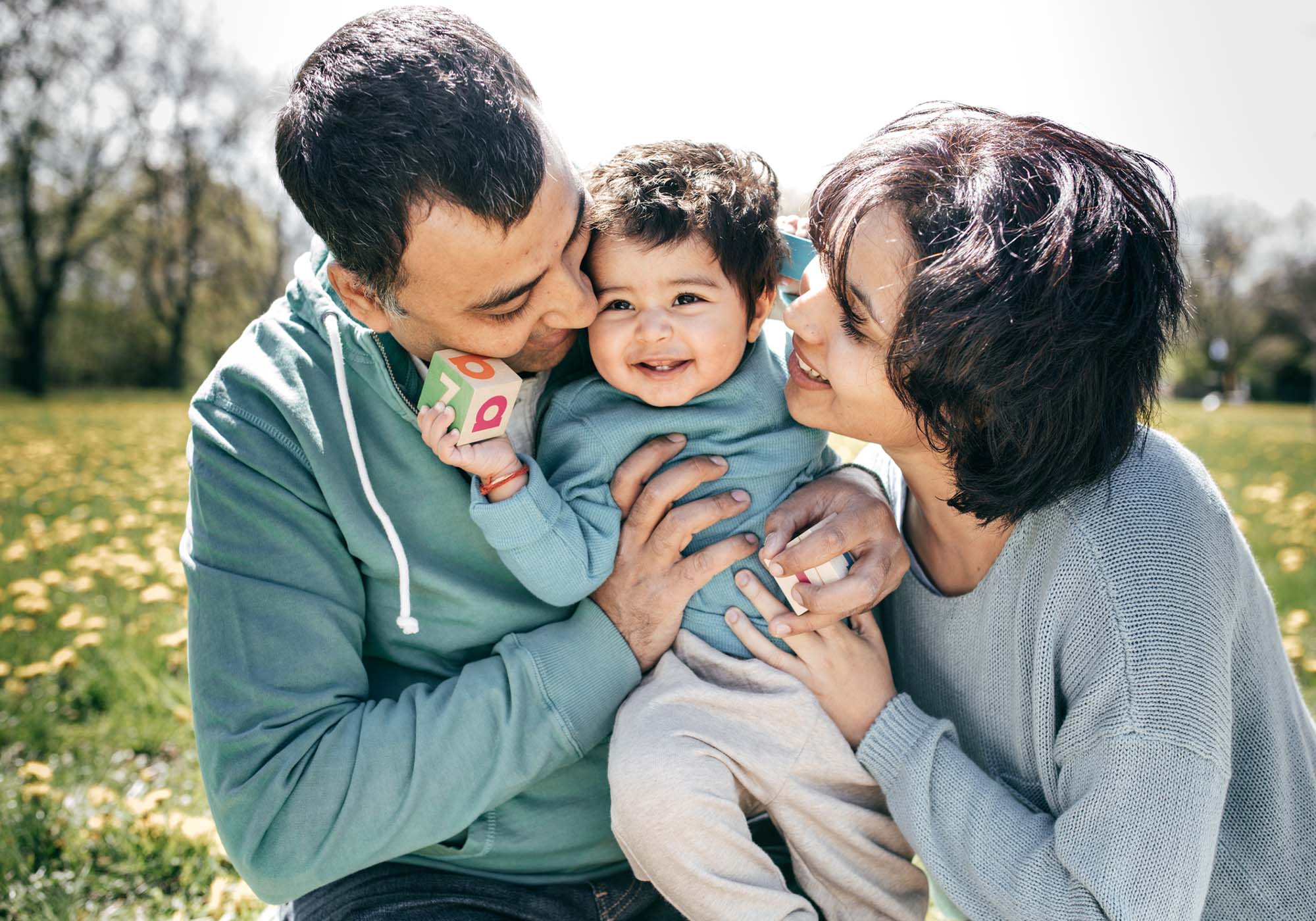 mom and dad kissing baby at the park