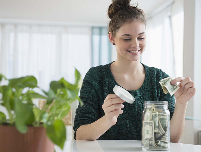 woman adding dollar to jar filled with cash