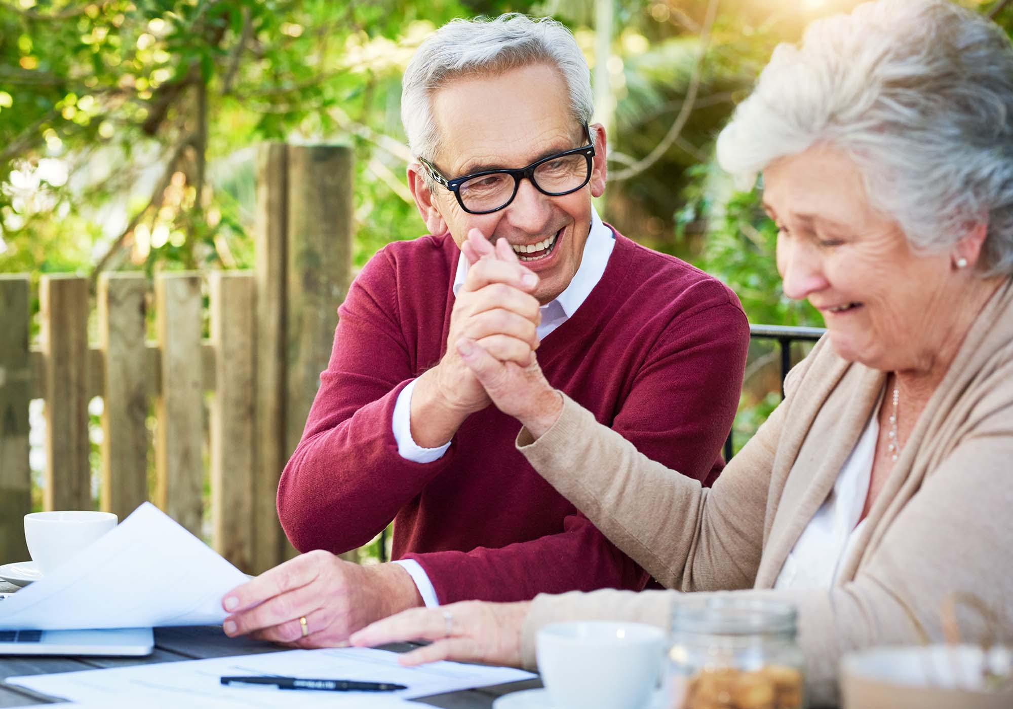 Elderly couple sitting outside looking at their bank statements and holding hands. 