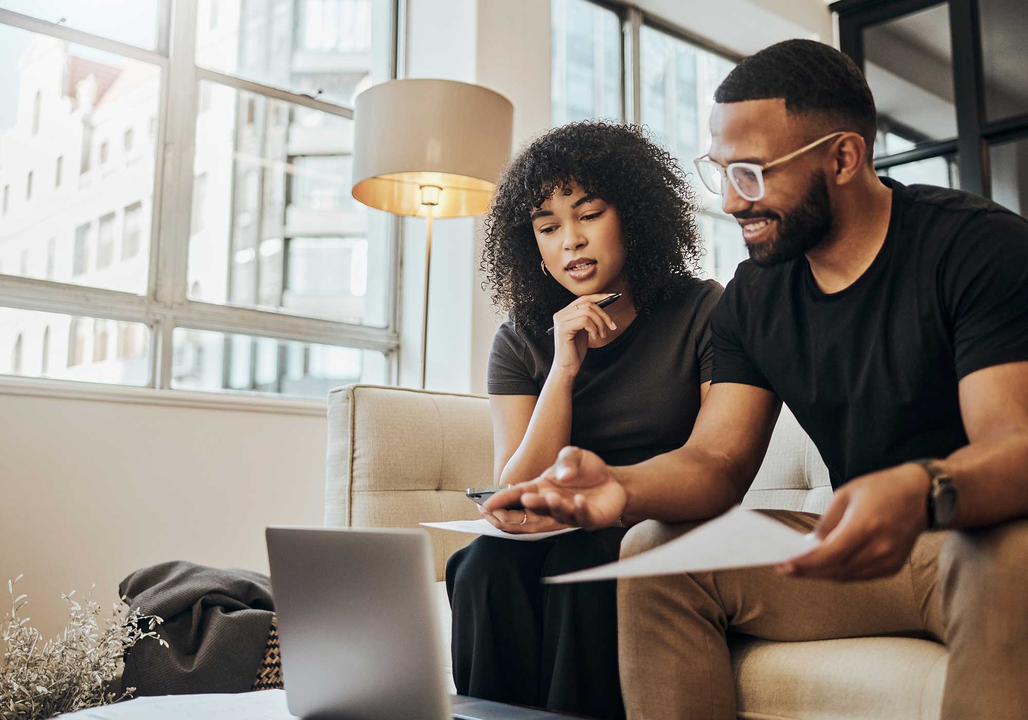 Couple sitting down at home, reviewing their finances on a laptop. 