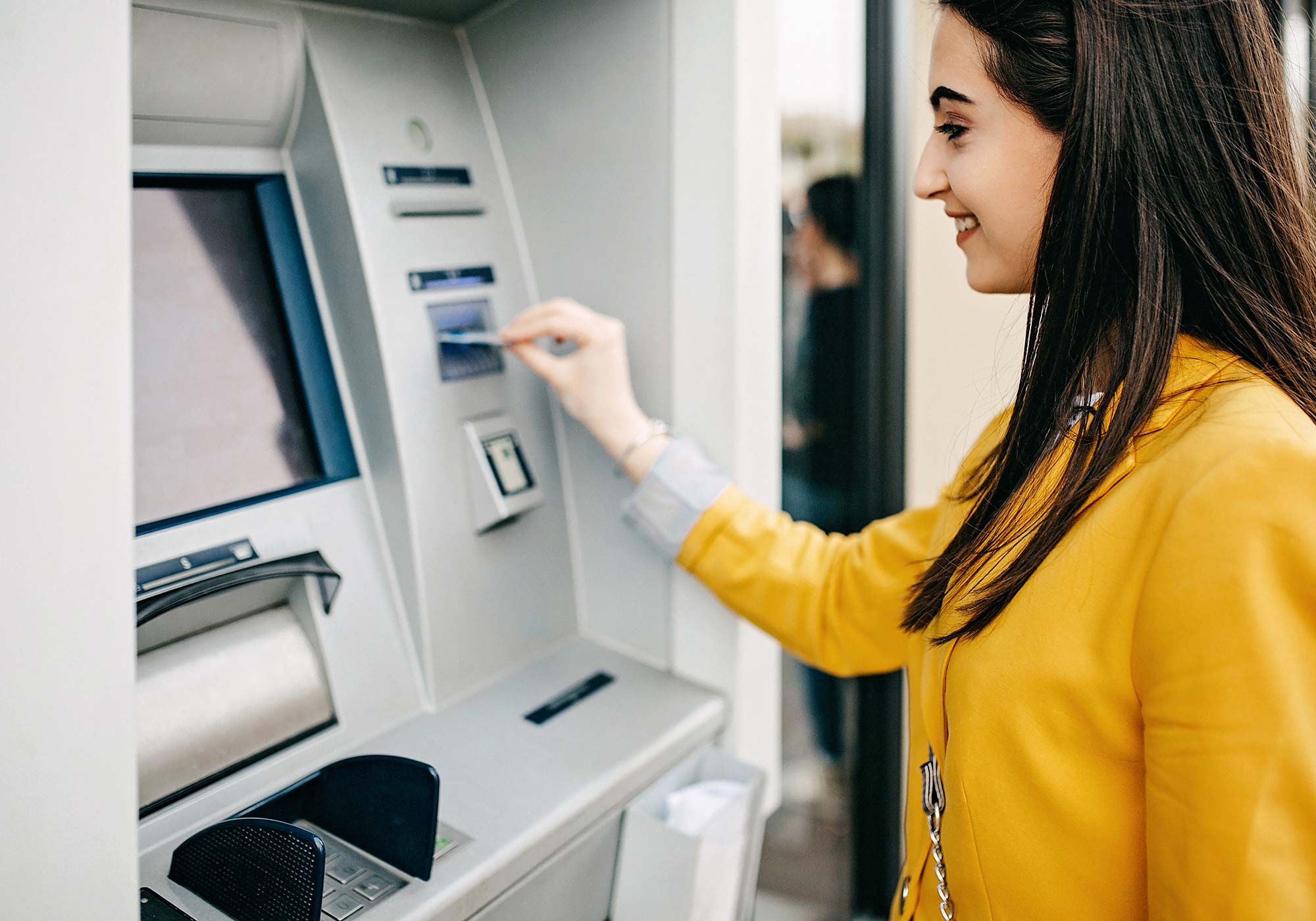 A woman smiling while inserting her The Police Credit Union card into an ATM machine.