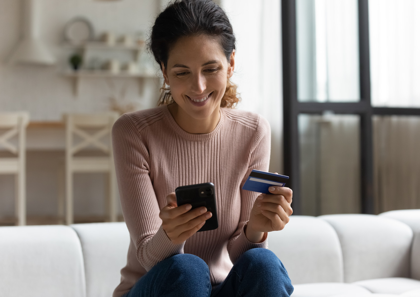 A woman sitting on her sofa holding her phone and The Police Credit Union card.