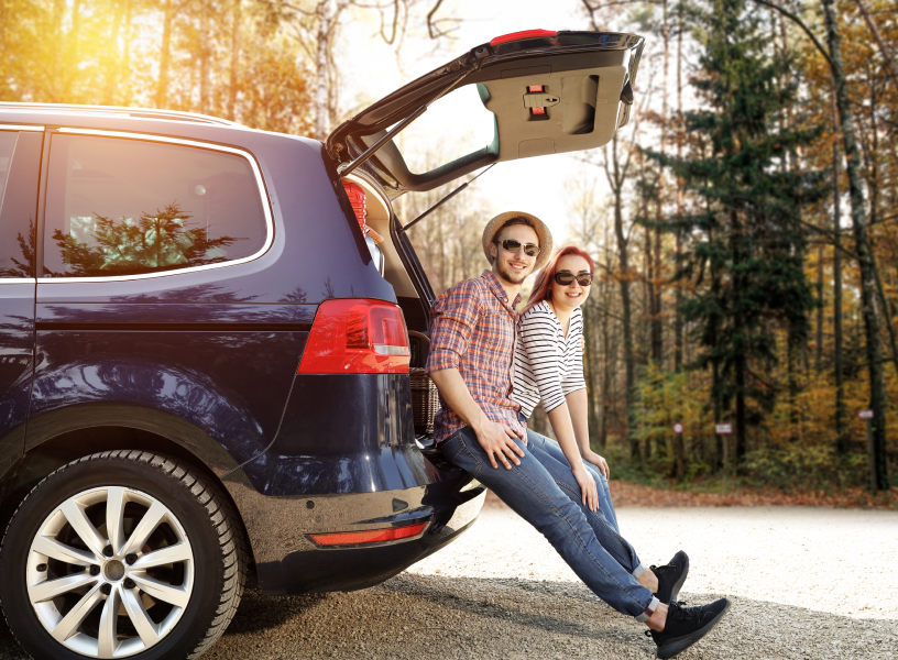 couple leaning against blue SUV next to tall trees