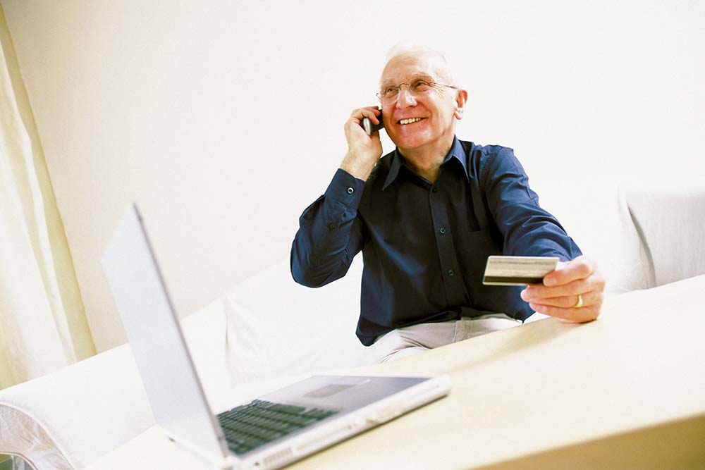 elderly man on phone while holding credit card 