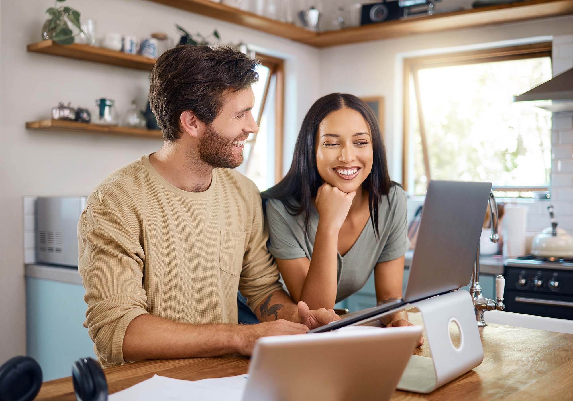 A happy couple in the kitchen reviewing their bank statements on a laptop. 