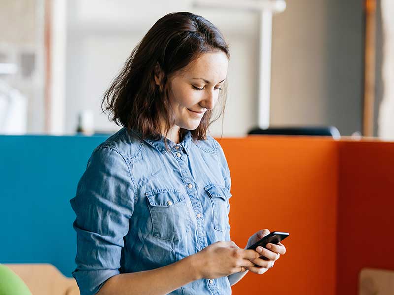 Woman wearing denim shirt, checking her The Police Credit Union Digital Banking account on her phone. 